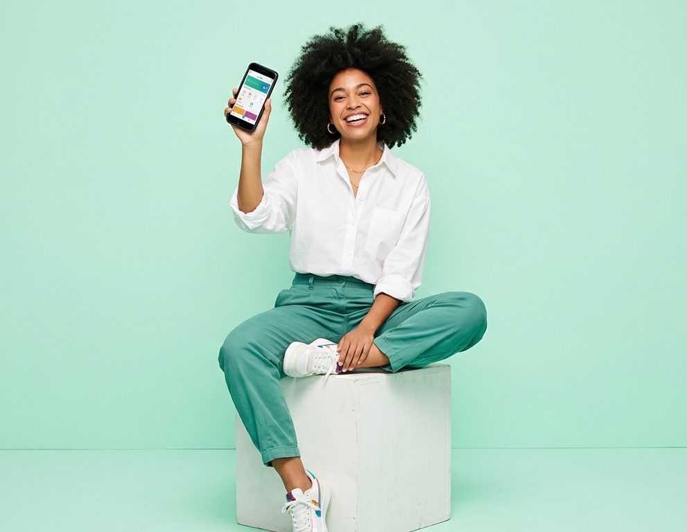 Smiling woman holding up her phone against a soft mint backdrop
