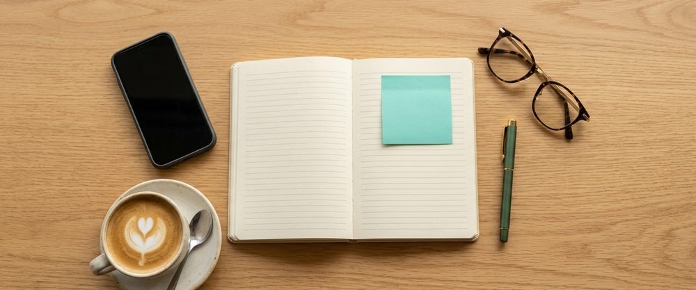 Open diary, coffee, phone and glasses on a timber table